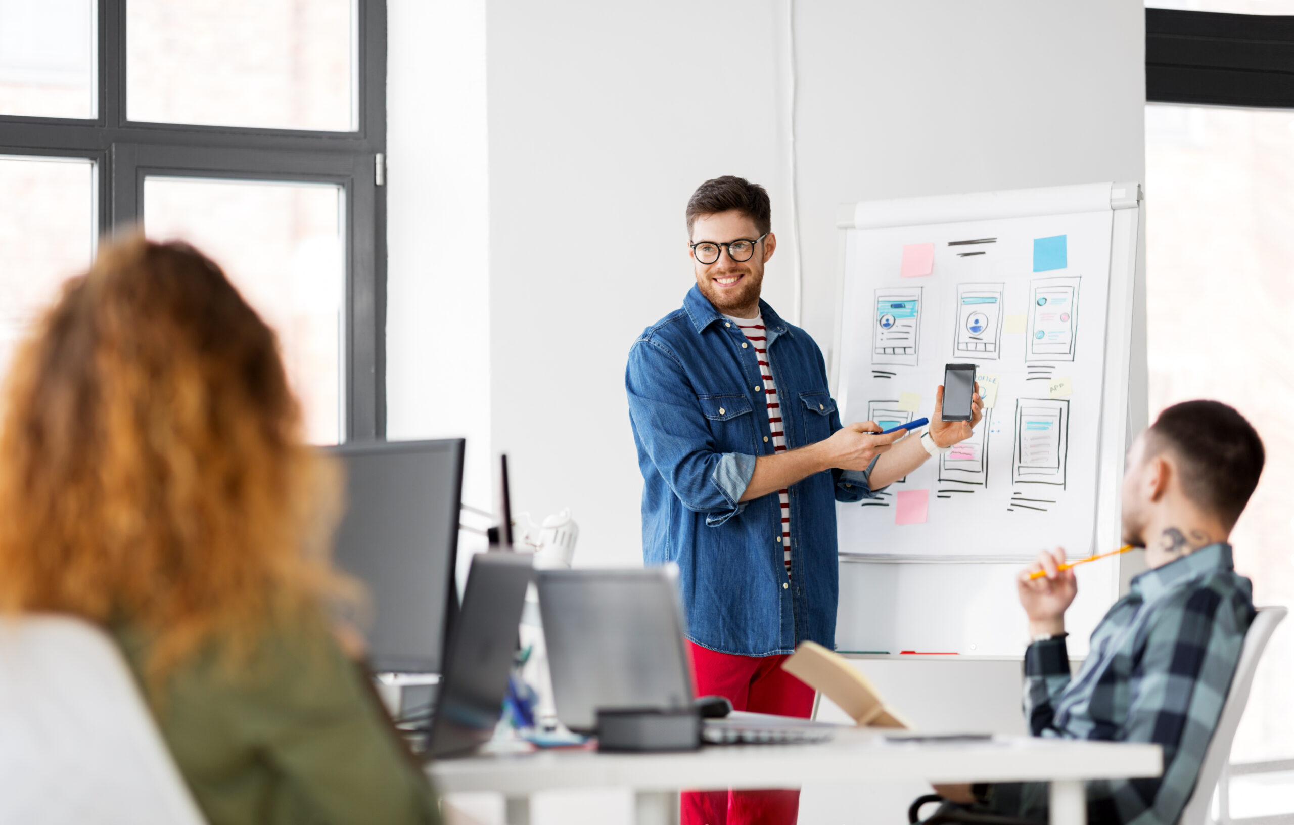 business, technology and people concept - man showing smartphone user interface design to creative team at office presentation