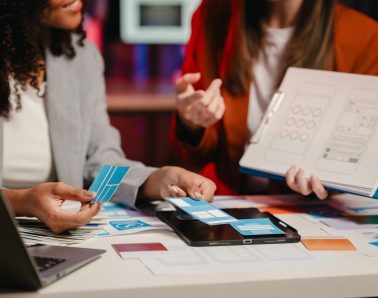 African American business worker with an afro presenting a UX,UI design on a clipboard to a Caucasian colleague in an office setting.
